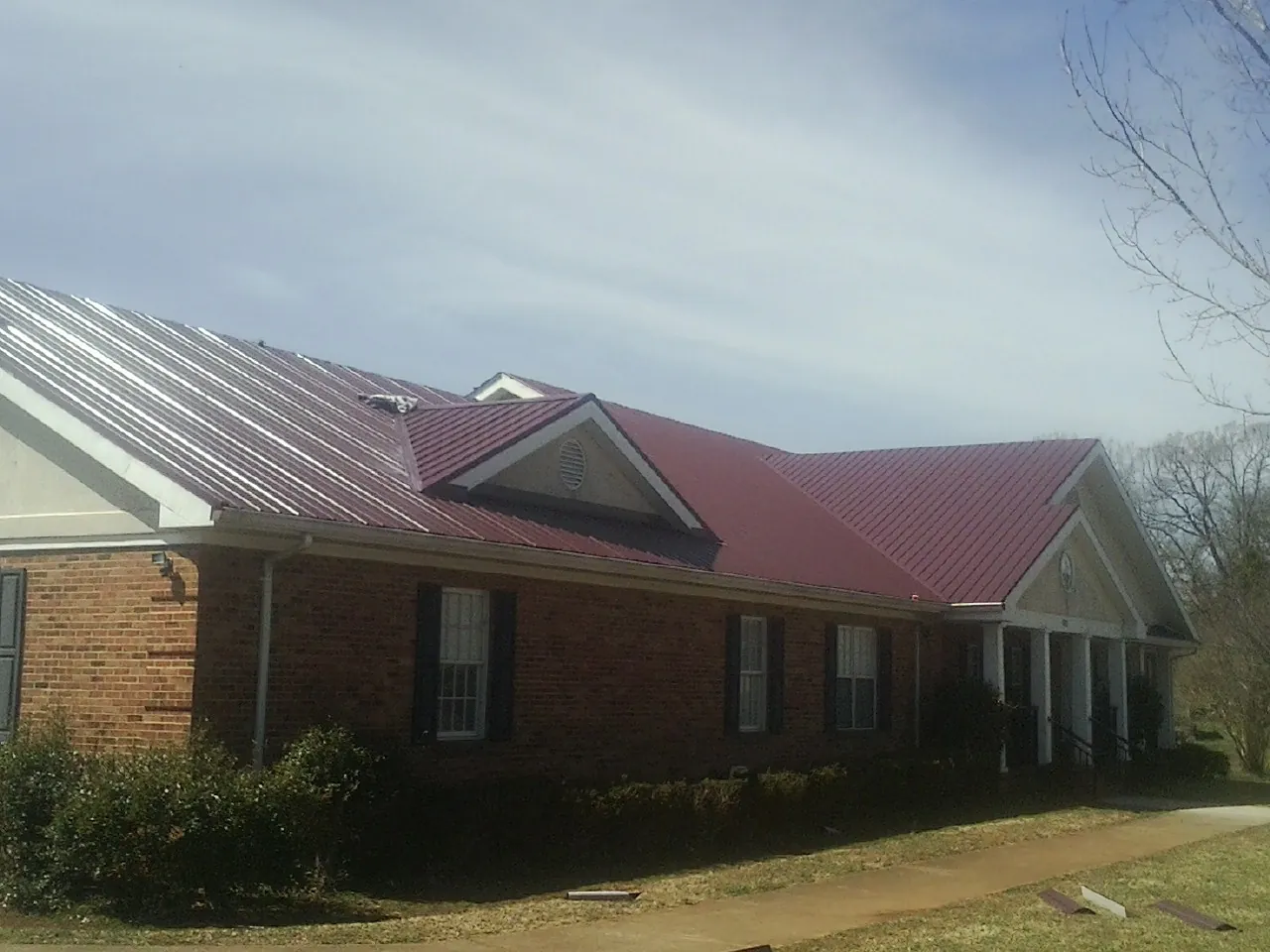 Red metal roof with gabled entries on a long brick building, from a Hail Damage Roof Repair job in Point Roberts