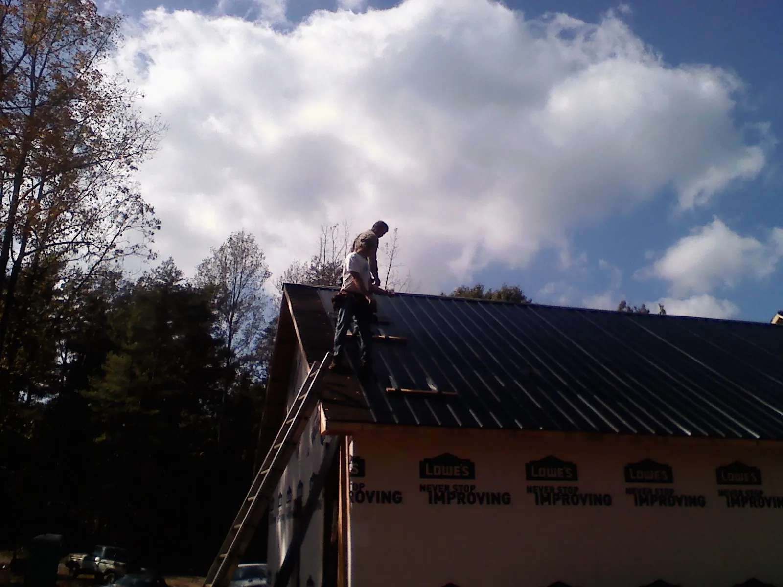 Roofer fastening dark metal panels high against a cloudy sky, from a Roof Inspection job in Point Roberts